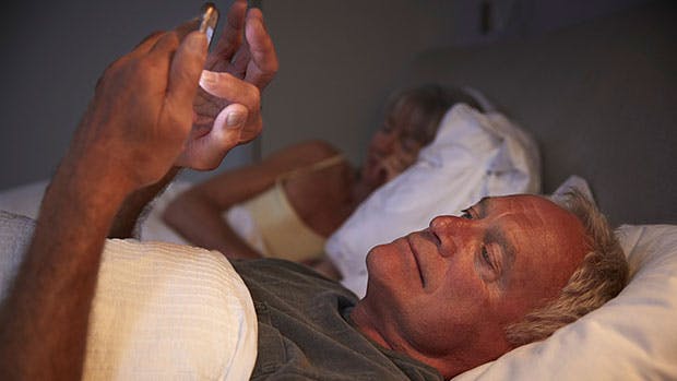 Mand ligger i sengen og tjekker sin kones telefon