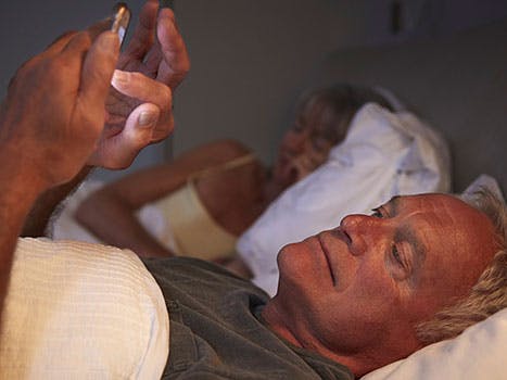 Mand ligger i sengen og tjekker sin kones telefon