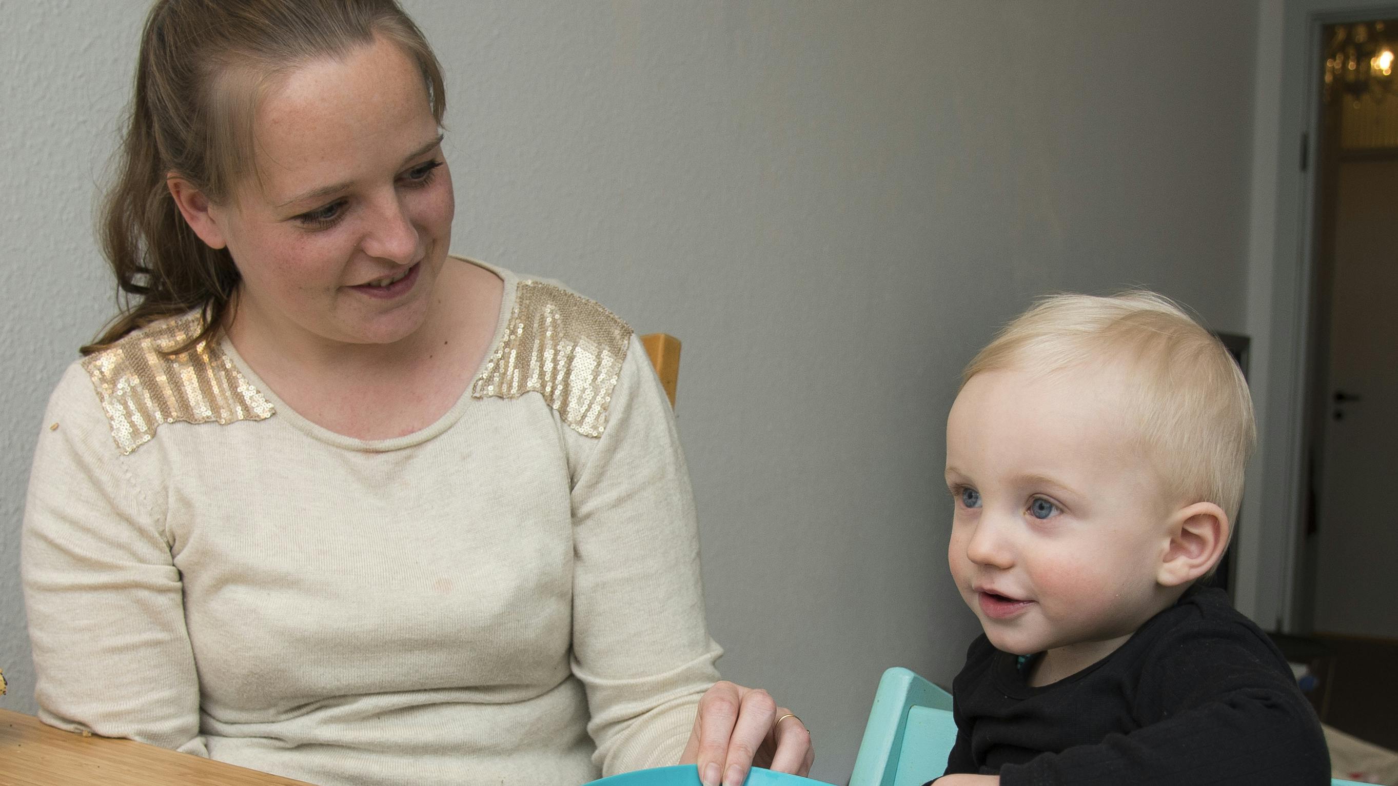 En ung mor og et lille barn i højstol sidder ved et spisebord