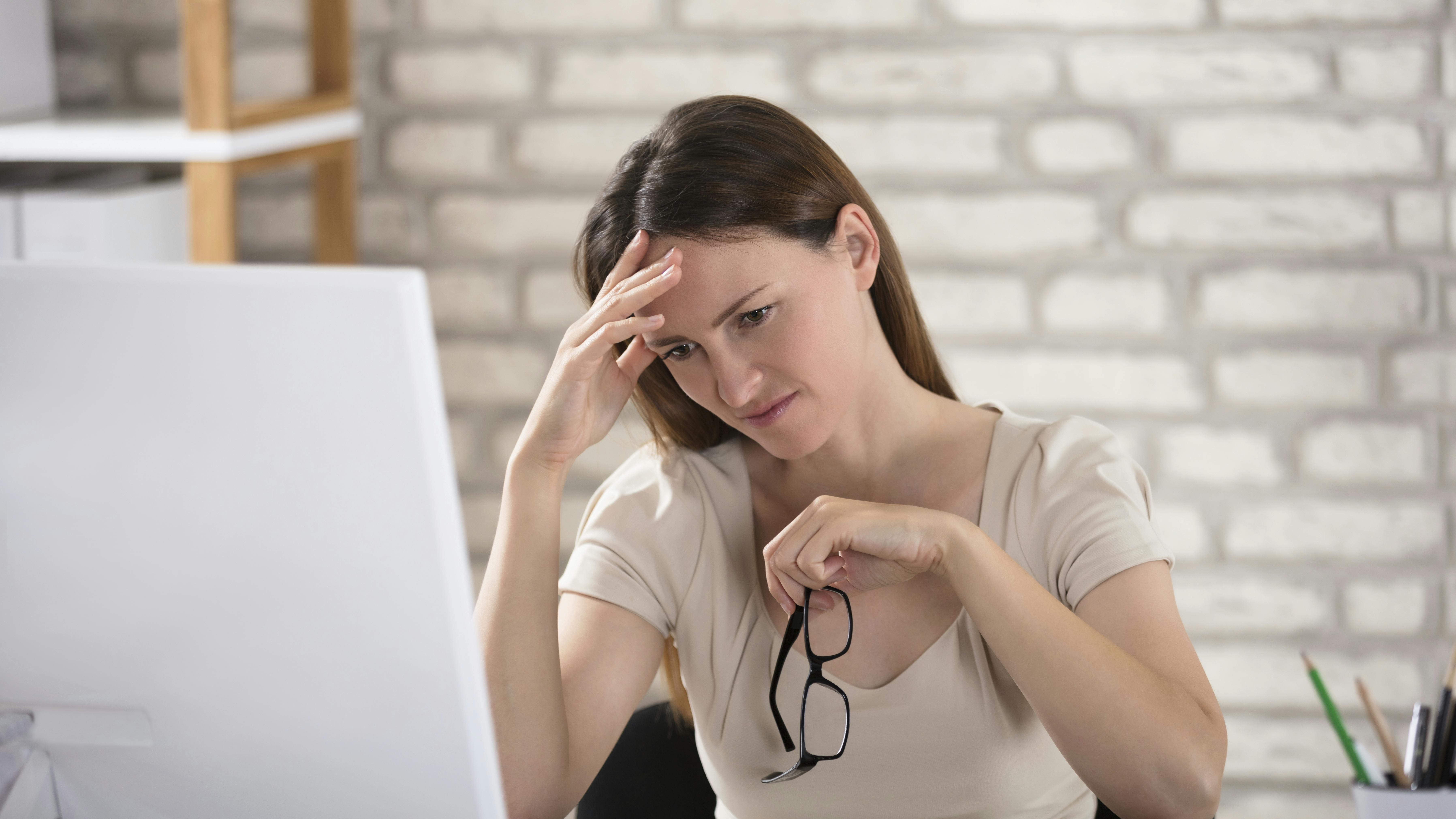Kvinde sidder foran computer og tager sig på hovedet