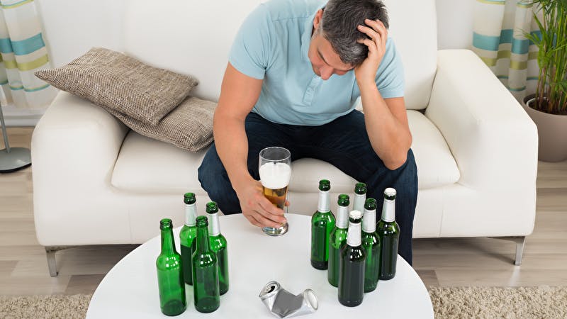 Alkoholiker sidder ved bord med flasker
