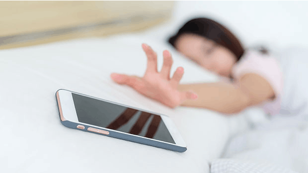 Test: Mobilafhængighed. Kvinde ligger i sengen og rækker ud efter mobiltelefon.