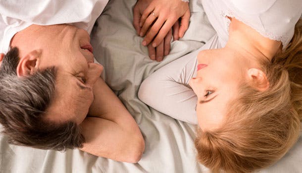 Kvinde og mand ligger på sengen og holder i hånd