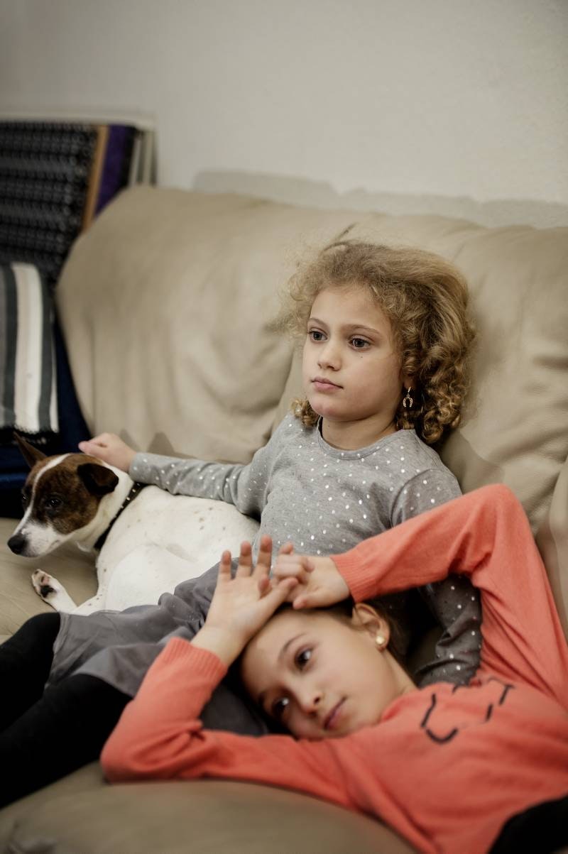 Sarah på 8 år og Yasmin på 6 år sidder sammen i en sofa med deres lille hund Mille